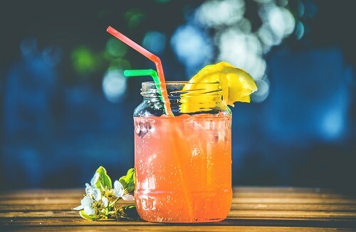 Cocktails with Orange Juice - A picture of an orange cocktail with orange juice in a jam jar glass, with a slice of lemon and two straws.