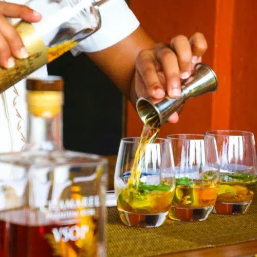 Bartender measuring spirits with a jigger into cocktail glasses